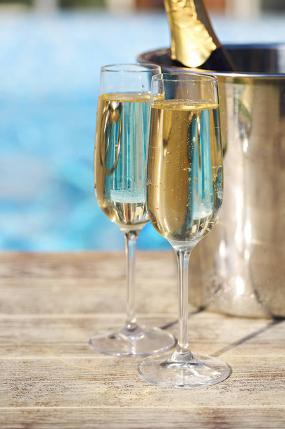 Champagne glasses and bottle in ice bucket near swimming pool. Vacation and romance concept - Photo, Image