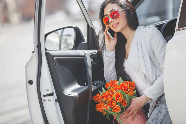 Atrakcyjna młoda kobieta rozmawia przez telefon komórkowy w pobliżu samochodu. Pewnie Pani o rozmowy telefon komórkowy. Kobieta w samochodzie. - Zdjęcie, obraz