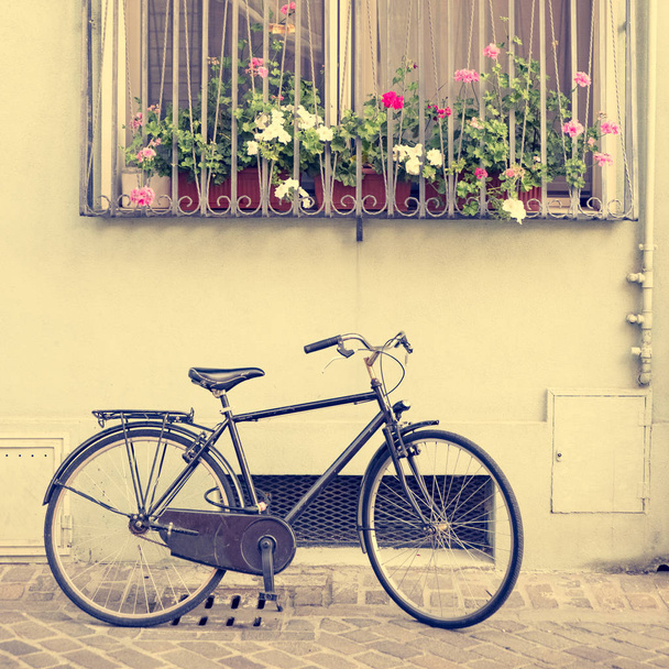 Vintage bicycle near the house with a window and flowers on the windowsill, square format. Toned. - Фото, изображение