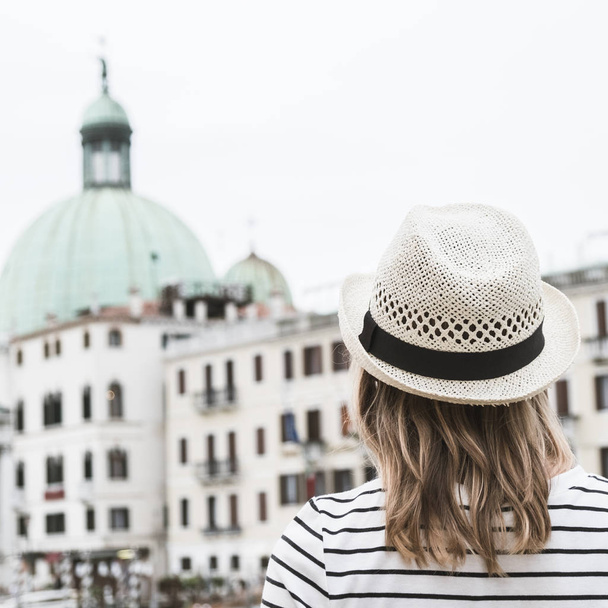 Dziewczyna w białej letni kapelusz stoi tyłem i patrzy na architekturze Wenecji, format kwadratowy. Stonowanych. - Zdjęcie, obraz