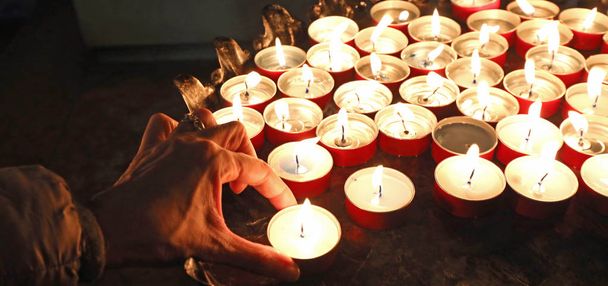 mano della vecchia vedova che prega con le tante candele accese nel luogo di culto
 - Foto, immagini