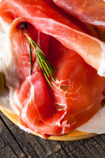 Closeup of thin slices of prosciutto with mixed olives and paprika on wooden cutting board - Photo, Image