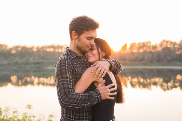 Ρομαντική και άνθρωποι έννοια - νεαρό ζευγάρι αγκάλιασμα μαζί κοντά στο ποτάμι ή λίμνη και απολαμβάνοντας την θερινή ώρα - Φωτογραφία, εικόνα