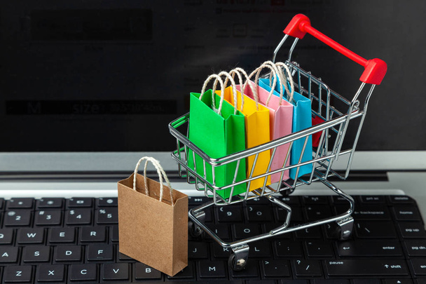 Het kopen van goederen en kleding in de online winkel. Winkelen zakken in de winkelwagen op laptop toetsenbord - Foto, afbeelding