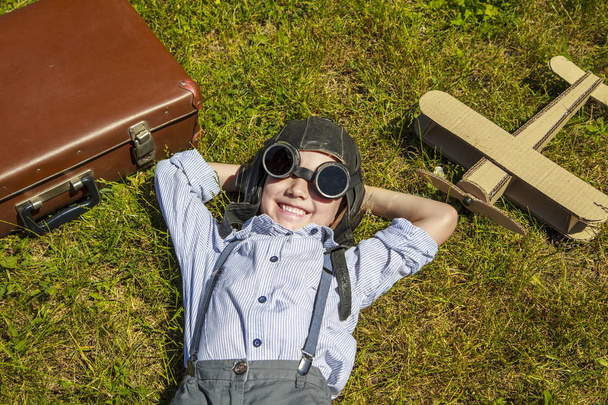 Ένα αγόρι με ένα αεροπλάνο, ευτυχισμένο παιδί ονειρεύεται να γίνει πιλότος, ξαπλωμένη στο γρασίδι. - Φωτογραφία, εικόνα