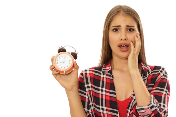 Young woman looking terrified screaming with her hand to her face holding alarm clock isolated on white copy space. Time management, timing, being late concept. Beautiful woman looking shocked - Photo, Image