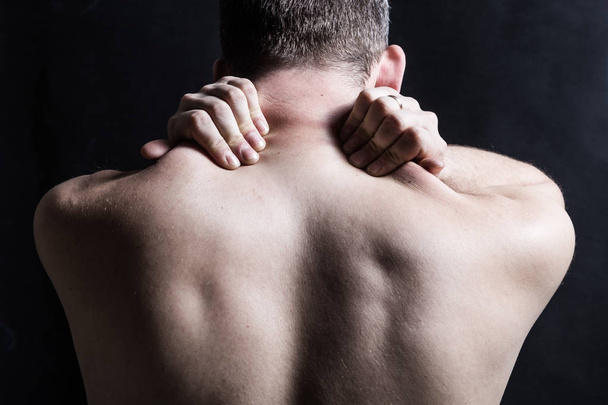 Ένας άντρας με πόνο στην πλάτη και στο λαιμό. Κοντινό κράτημα στο λαιμό σε σκούρο φόντο. - Φωτογραφία, εικόνα