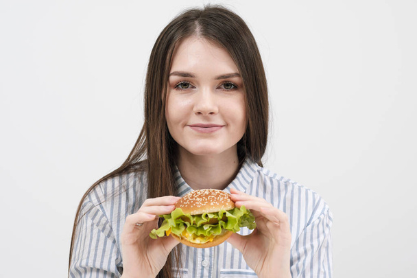 Стройная брюнетка держит в руках гамбургер. На белом фоне, тема диеты и правильного питания
, - Фото, изображение
