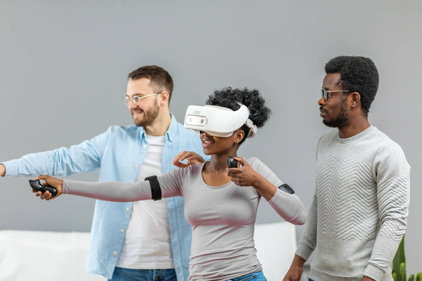 Two guys help african woman trying on virtual reality glasses for the first time - Foto, immagini