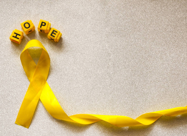 golden ribbon and words made up of children's plastic beeches. concept - a symbol of childhood cancer, pediatric oncology. - Foto, imagen