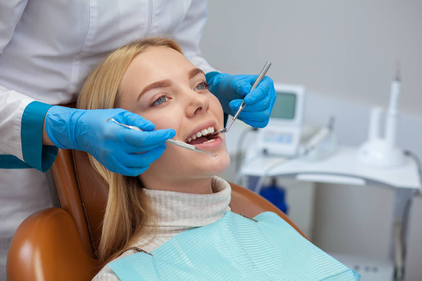 Tiro cortado de um dentista profissional examinando os dentes de uma bela jovem. Mulher atraente sorrindo, enquanto dentista checando os dentes. Consulta dentária na clínica. Medicina, saúde
 - Foto, Imagem