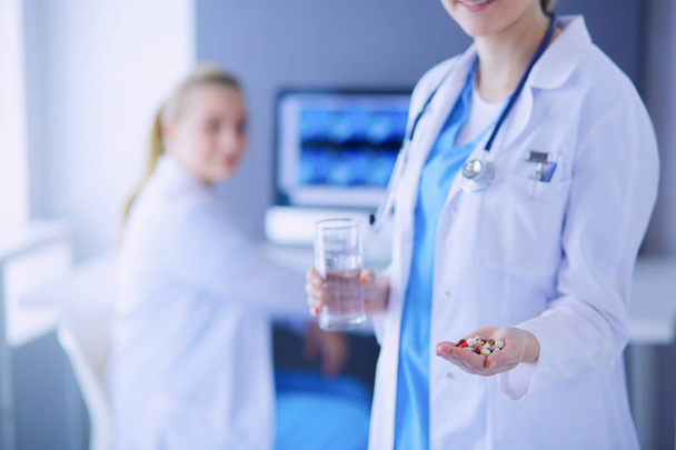 shot of doctor holding pills and glass of water at clinic with colleague on the background. - Foto, Bild
