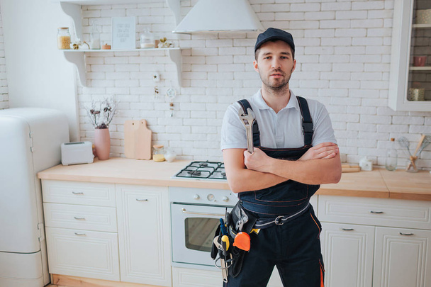 Plumber in kitchen. Professional look on camera and pose. Hands crossed. Tools on belt aside. - Fotoğraf, Görsel