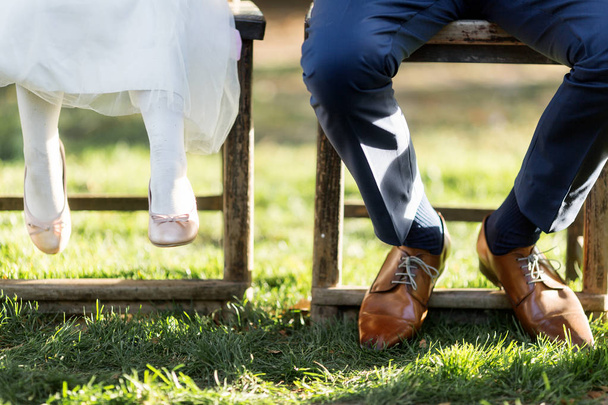 pés masculinos em sapatos de couro elegantes e pés de menina sentada em cadeiras ao ar livre
 - Foto, Imagem