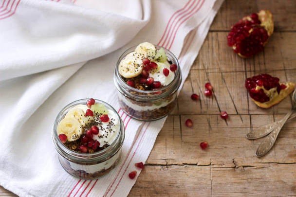 Granola con yogurt e frutta in barattoli di vetro su un tavolo di legno. Stile rustico, attenzione selettiva
. - Foto, immagini