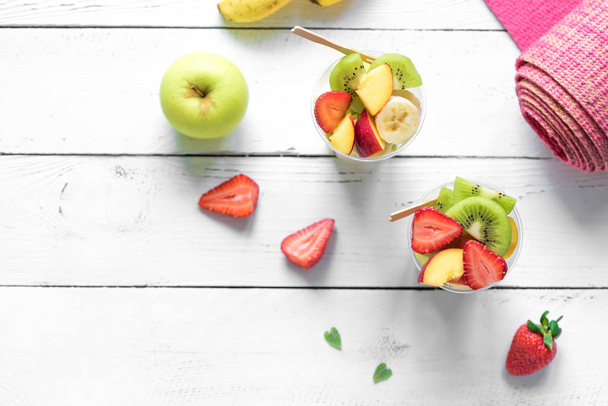 Feminine Sport and Healthy Lifestyle Concept. Pink yoga mat and Fruit and Berries Salad in plastic cup to go, copy space, top view. - Zdjęcie, obraz