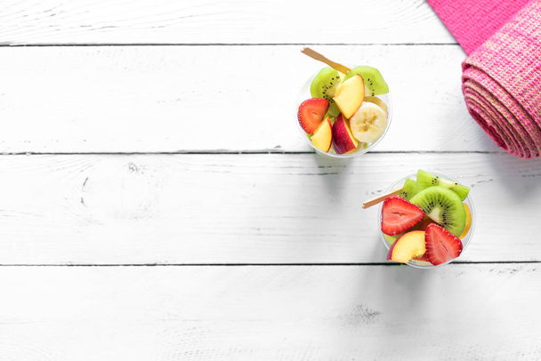 Feminine Sport and Healthy Lifestyle Concept. Pink yoga mat and Fruit and Berries Salad in plastic cup to go, copy space, top view. - Foto, afbeelding