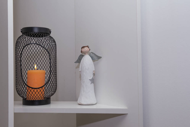 lamppu, jossa on kuohuviini kynttilä, seisoo kevyellä hyllyllä enkelin patsaan lähellä
  - Valokuva, kuva