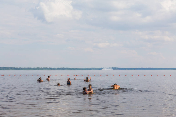 Saratow / Russland - 7. Juli 2018: Menschen schwimmen im Fluss am Strand. sonniger Sommertag. malerische Wolken am Himmel. Flusslandschaft. - Foto, Bild