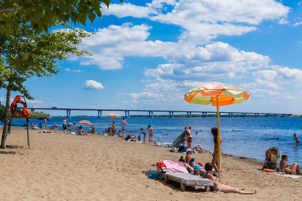 Saratov / Russia - July 5, 2018: People sunbathe and swim in the river on a sandy beach. On a Sunny summer day. Road bridge on the horizon. - Photo, Image