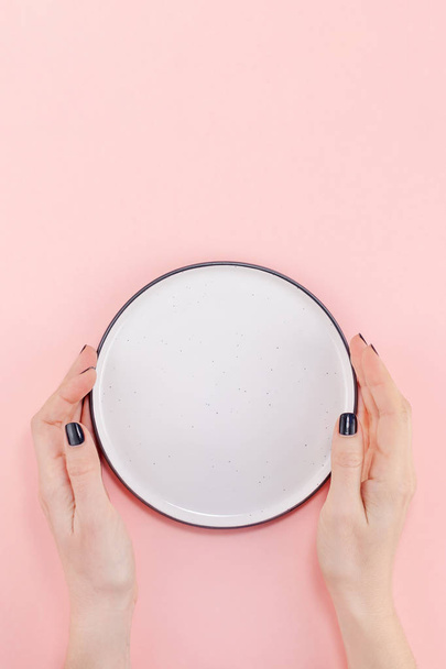 Креативный плоский вид сверху на женские руки черного маникюра с пустой тарелкой, намазанной на розовый бумажный фон копировального пространства. Минимальный шаблон концепции обслуживания блюд для оформления текстового меню
 - Фото, изображение