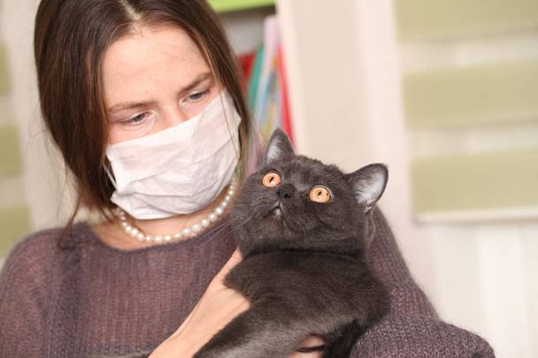 meisje in medische masker op haar gezicht houdt Britse kat breed.toxoplasmosis bescherming tegen kat infectie voor de mens. - Foto, afbeelding