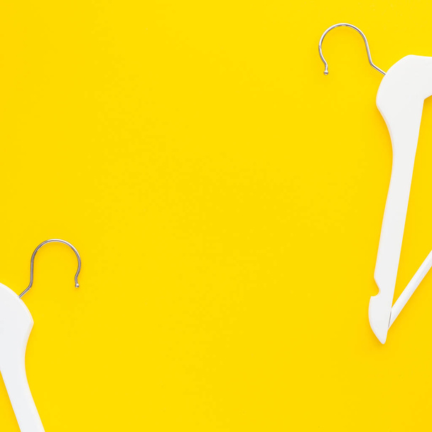 kreative Draufsicht flach lagen weiße Holzbügel isoliert fett gelben Hintergrund mit Kopierraum Minimalismus Stil. Vorlage Mode feminin blog social media verkauf shop promo design shopping konzept - Foto, Bild