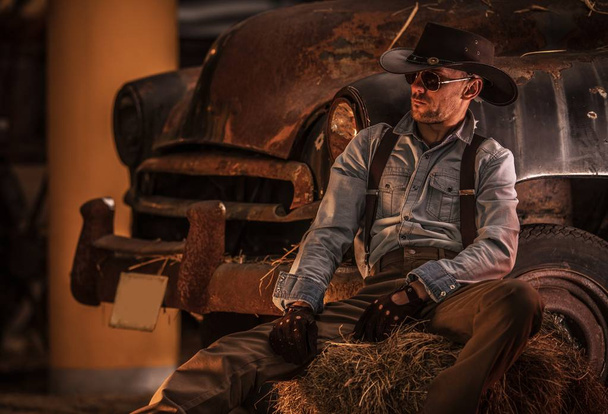 Caucasiano Cowboy em seus 30 e Rusty Classic Car Inside the Barn
. - Foto, Imagem