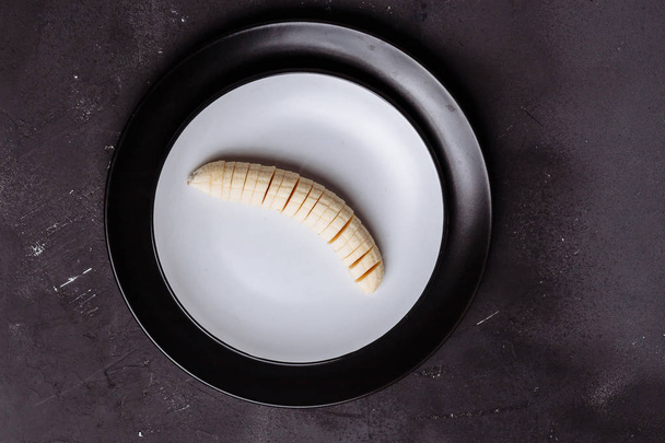Closeup of sliced banana in a plate on a black wooden background on a table, top view, flat lay - Zdjęcie, obraz