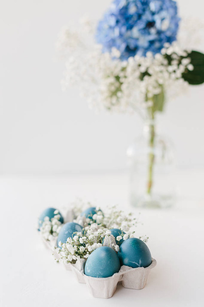 Blue natural colored easter eggs in tray with small white flowers baby breath gypsophila, blue hydrangea flower in vase. Easter decoration - Photo, image