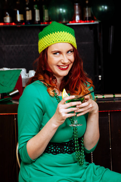 La ragazza festeggia il giorno di San Patrizio. Le donne si divertono al bar. Una bella ragazza con un cappello verde e vestito beve un cocktail verde
. - Foto, immagini