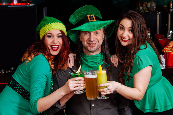 The company of young girls and one man celebrate St. Patrick's Day. They have fun at the bar. They are dressed in carnival headgear, green hats and clothes. - Фото, зображення