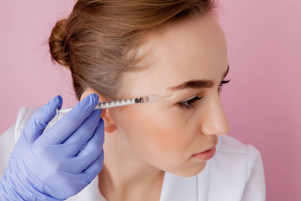The doctor cosmetologist makes the Botulinotoxin injection procedure for tightening and smoothing wrinkles on the face skin of a beautiful, young woman in a beauty salon.Cosmetology skin care. - Foto, immagini