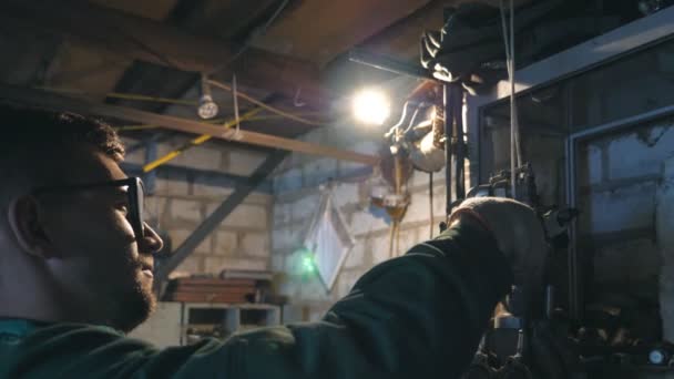 Mechanic doing his work using tool. Man in workwear works in garage or workshop. Profile of young male repairer in glasses. Hard work concept. Dolly shot Slow motion Close up - Footage, Video