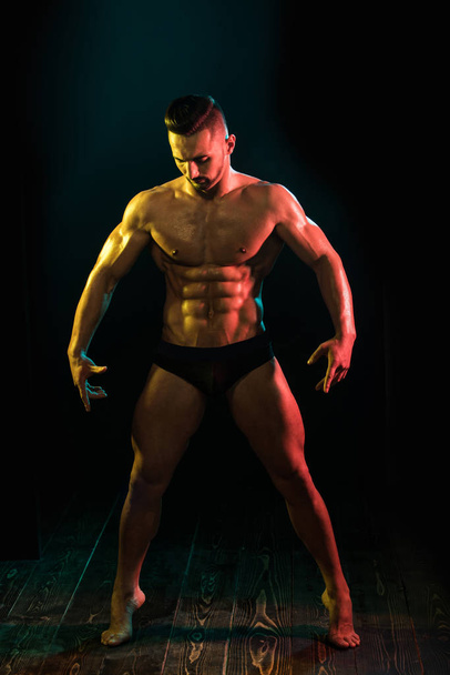 Σπορ άνθρωπος που δείχνει στα ανοικτά του μυϊκή διάπλαση και έξι pack abs. φωτογραφία νεαρού άνδρα με τέλειο σώμα μετά την προπόνηση σε μαύρο φόντο. - Φωτογραφία, εικόνα