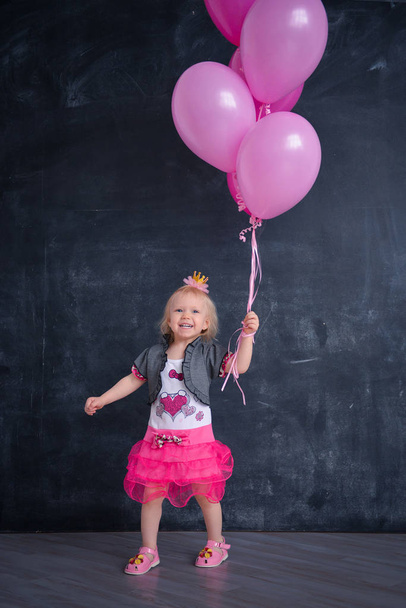 themed birthday for a fun emotional girl of the blonde smash the cake in pink color on a black background. stylized photo session tradition with sweet decor and balloons - Foto, Imagem