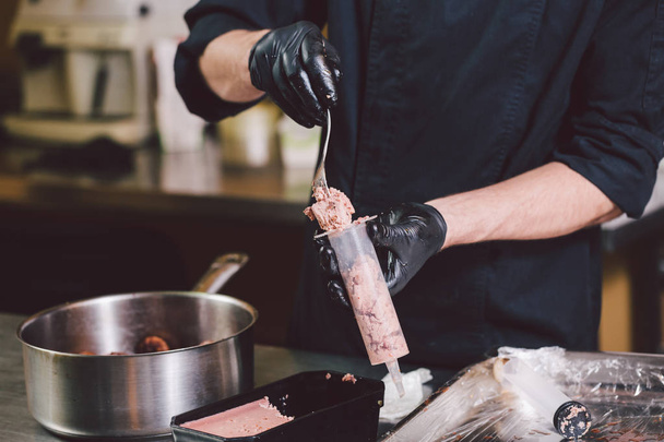Theme cooking. Hands close up. young Caucasian man in black uniform and latex gloves in kitchen. restaurant prepares ground beef and leads into berry with syringe. Dish of figs, figs or Carian ficus. - Foto, Imagen