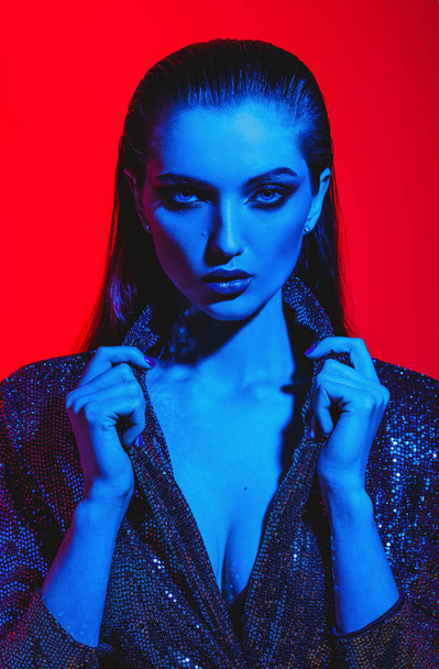 Fashion girl with long hair and stylish makeup in a black shining dress poses on the red background in neon light in the studio - Fotoğraf, Görsel