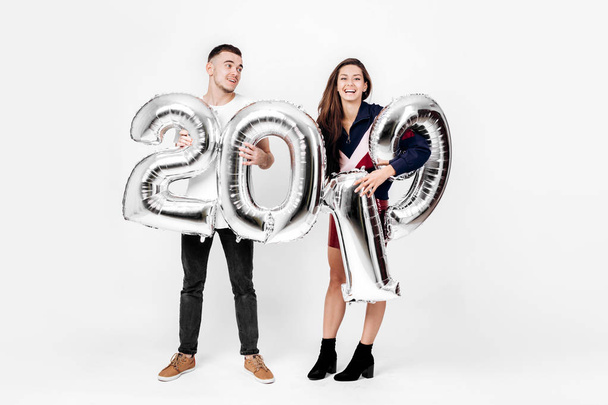 Smiling girl and guy dressed in a stylish clothes are having fun with balloons in the shape of numbers 2019 on a white background in the studio - Valokuva, kuva