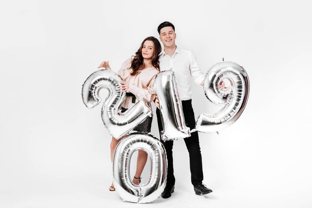 Girl and guy dressed in a stylish smart clothes are holding balloons in the shape of numbers 2019 on a white background in the studio - Φωτογραφία, εικόνα