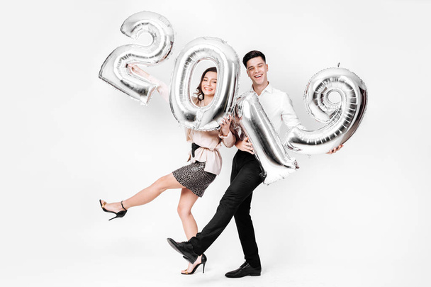 Funny girl and guy dressed in a stylish smart clothes are holding balloons in the shape of numbers 2019 on a white background in the studio - Φωτογραφία, εικόνα