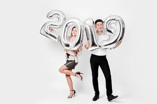 Funny girl and guy dressed in a stylish smart clothes are holding balloons in the shape of numbers 2019 on a white background in the studio - Fotoğraf, Görsel