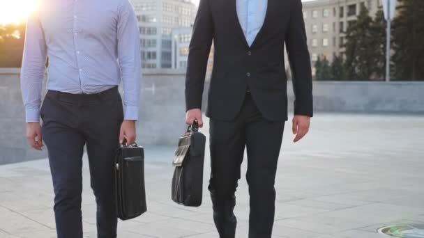 Two businessmen with briefcases walking in city street with sun flare at background. Partners commute to work together. Confident guys being on his way to office. Colleagues going outdoor. Slow mo - Footage, Video