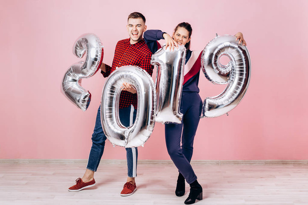 Funny friends girl and guy dressed in stylish clothes are holding balloons in the shape of numbers 2019 on a pink background in the studio - Fotó, kép
