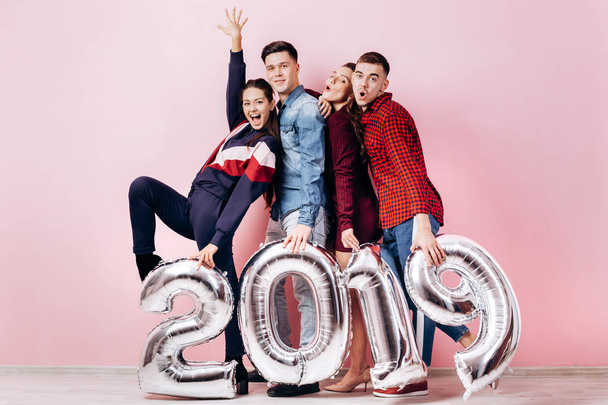 Boldog vállalat, a két lány és két srác öltözött elegáns ruhákat tartja lufi alakú számok 2019 egy rózsaszín háttér, a stúdióban - Fotó, kép