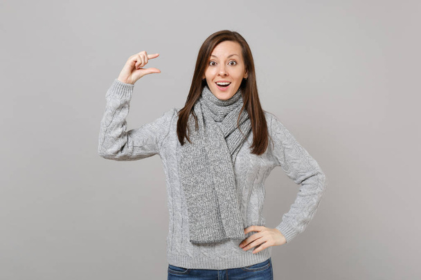 Excited woman in gray sweater scarf gesturing demonstrating size with copy space isolated on grey background. Healthy fashion lifestyle people sincere emotions cold season concept. Mock up copy space - Zdjęcie, obraz