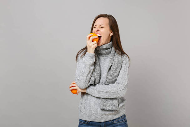 Молода жінка в сірому светрі, шарф тримає кусаючий апельсин ізольовано на сірому фоні стіни, студійний портрет. Здоровий спосіб життя, щирі емоції, концепція холодного сезону. Збільшити простір для копіювання
 - Фото, зображення