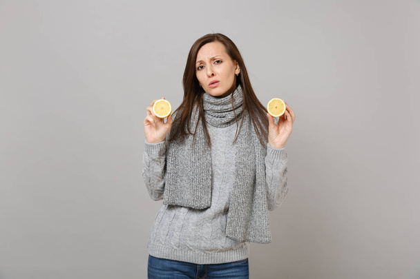 Tired sad young woman in gray sweater, scarf hold lemons isolated on grey wall background, studio portrait. Healthy fashion lifestyle, people sincere emotions, cold season concept. Mock up copy space - Photo, Image