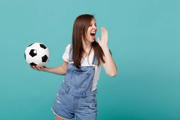 Gek meisje voetbalfan vrolijken favoriete ondersteuningsteam met voetbal schreeuwen met handgebaar geïsoleerd op blauwe turkooizen achtergrond in de studio. Emoties van de mensen sport familie leisure concept - Foto, afbeelding