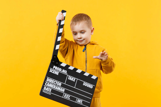 Little kid boy 3-4 years old in yellow clothes isolated on orange wall background, children studio portrait. People childhood lifestyle concept. Hand hold film making clapperboard. Mock up copy space - Fotoğraf, Görsel
